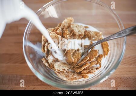 Auf einem Holztisch befindet sich eine klare Glasschüssel mit Haferflocken, die mit Milch gefüllt ist. Köstliches und leichtes Frühstück am frühen Morgen. Stockfoto