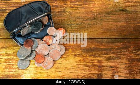 Offene schwarze Leder-Geldbörse voller verschiedener Münzen. Finanzkrise, Armut, Geldmangel. Auf Holzhintergrund oder Tisch. Flach liegend. Draufsicht. C Stockfoto