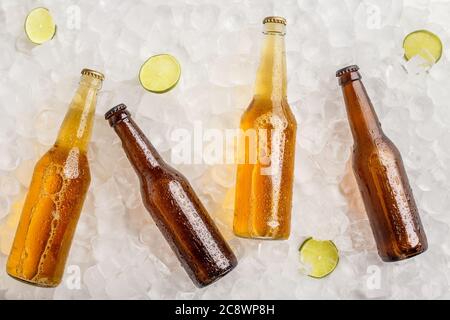 Verschiedene Biere gekühlt für Party. Kalte Glasflaschen mit Bier in Eis mit Limette Stockfoto