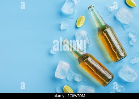 Zwei kalte Flaschen helles Bier ohne Etikett mit Eis und Limettenstücken auf blauem Hintergrund Stockfoto