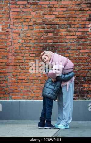 Liebevolle junge Mutter umarmt Schuljunge Hipster genießen Zeit zusammen in der Stadt Straße. Glückliche Familie alleinerziehende Mutter mit Sohn Spaß spielen fühlen Freude Kuscheln und Umarmung Stockfoto