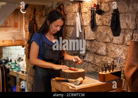 Lederhandlerin in ihrer stimmungsvollen Werkstatt an einem handgefertigten Gürtel. Konzept: Weiblicher handwerklicher Lebensstil Stockfoto