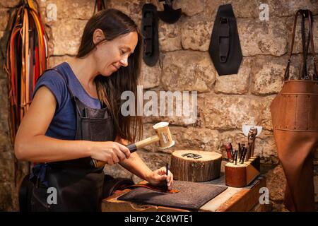 Lederhandlerin in ihrer stimmungsvollen Werkstatt an einem handgefertigten Gürtel. Konzept: Weiblicher handwerklicher Lebensstil Stockfoto