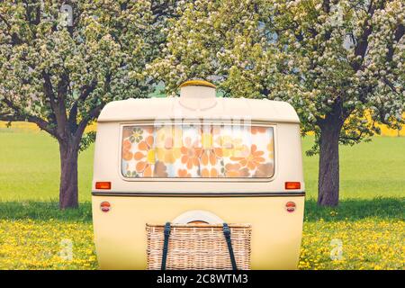 Vintage-Rückwand eines Caravans in zweifarbigen Gelb und Weiß vor einer holländischen Landschaft mit blühenden Blumen und blühenden Bäumen Stockfoto