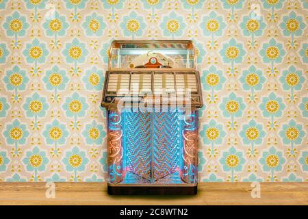 Bunte Vintage Jukebox vor Retro-Blumen-Tapete auf einem Holzboden Stockfoto