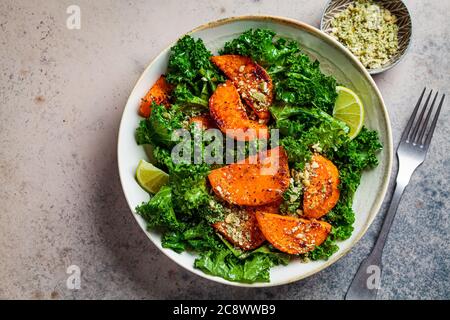 Gebackener Süßkartoffelsalat mit Grünkohl in einer Schüssel, dunkler Hintergrund. Veganes Lebensmittelkonzept. Stockfoto