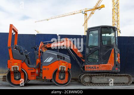 Rot gefärbte Bagger und Walzenverdichter stationär in der Nähe einer Baustelle, Kräne im Hintergrund geparkt. Karakoy, Istanbul / Türkei. Stockfoto