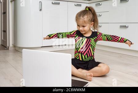 Das Mädchen 4 Jahre alt in einem Turnanzug ist in rhythmischen Gymnastik online zu Hause beschäftigt und schaut in einen Laptop Stockfoto