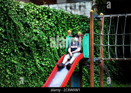 Boy saß allein auf Folie trägt Gesichtsmaske, Barcelona. Stockfoto