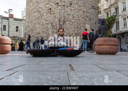 Junge Straßenmusiker spielen Hangdrum unter Galata Tower, während Touristen erkunden Galata Tower im Hintergrund. Beyoglu, Istanbul / Türkei. Stockfoto