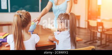 Geografie-Lehrerin zeigt zwei Schülerinnen auf einer Welt, Einzelunterricht, Wahlfach Stockfoto