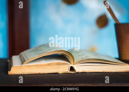 Öffnen Sie das Buch auf einem Tisch mit abstraktem Hintergrund im Herbst am Fenster für eine gemütliche Lesezeit zu Hause Stockfoto