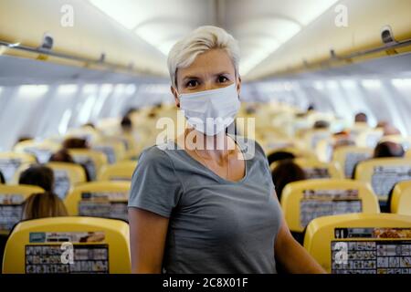Frau im Flugzeug mit Schutzmaske umgeben von vielen sitzenden Menschen Stockfoto