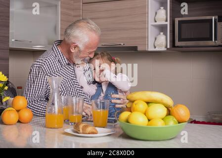 Älterer Mann und seine entzückende Enkelin trinken frischen Orangensaft Und Spaß in der Küche Stockfoto