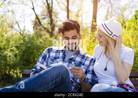 Glückliches kaukasisches Paar, das auf einer Parkbank sitzt und zusammen ein Buch liest Stockfoto