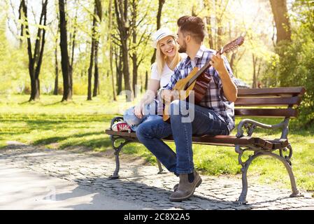 Junges Paar Gitarre spielen und Spaß zusammen auf einem parkbank Stockfoto