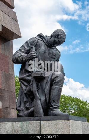 Bronzeskulptur eines knienden Soldaten, der Waffe und Helm vor einer abstrakten Granitfahne am sowjetischen Kriegsdenkmal im Treptow Park, Berlin, hält Stockfoto