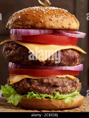 Doppelter Cheeseburger mit Tomaten, Zwiebeln, Grillschnitzel und Sesambrötchen auf einem alten Holzschneidebrett. Fast Food, Nahaufnahme Stockfoto