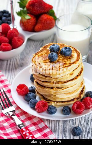 Stapel von Pfannkuchen mit frischer Heidelbeere und Himbeere, mit Honig gegossen. Milch und frische Beeren, gesundes Frühstückskonzept Stockfoto