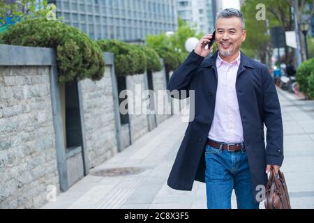 Outdoor-Tragen einer Aktentasche auf dem Telefon Geschäft in mittleren Alters Männer Stockfoto