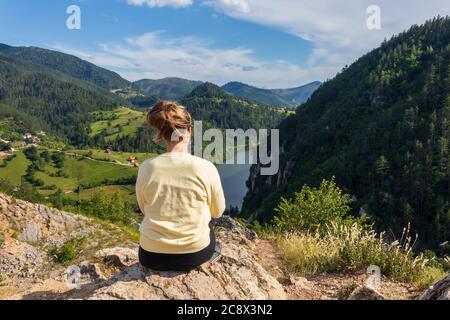 Junges Mädchen in der Natur. Rückansicht Porträt einer alleinerziehenden Frau, die den Spajici See aus der Höhe in Westserbien beobachtet Stockfoto