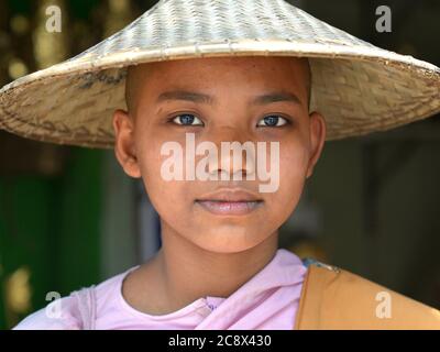 Junge burmesische buddhistische Nonne mit rasierten Kopf trägt einen traditionellen asiatischen konischen Hut. Stockfoto