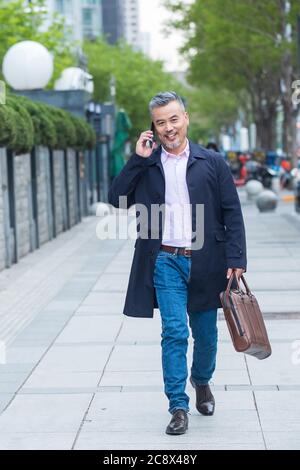 Outdoor-Tragen einer Aktentasche auf dem Telefon Geschäft in mittleren Alters Männer Stockfoto