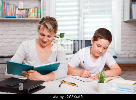 Mutter hilft Sohn, Unterricht zu machen. Der Tutor ist mit dem Kind beschäftigt Stockfoto