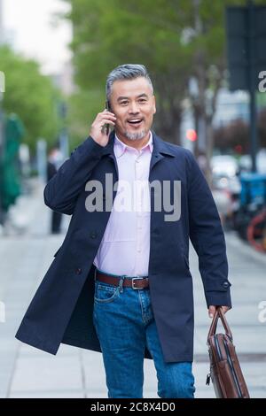 Outdoor-Tragen einer Aktentasche auf dem Telefon Geschäft in mittleren Alters Männer Stockfoto