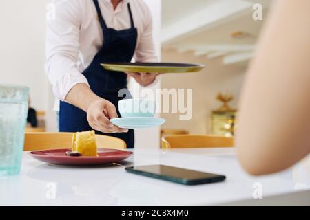 Nahaufnahme des Kellners, der Teller mit Dessert und Tasse Kaffee vor der Kundin legt Stockfoto