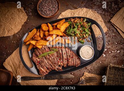 Rindersteak und Kartoffeln mit Pfeffersauce und Salat auf schwarzem Teller, Draufsicht Stockfoto