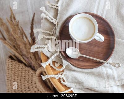 Eine Kaffeetasse mit Milch auf einem Holzteller und getrockneten Bentgrasen in einem Korb Stockfoto