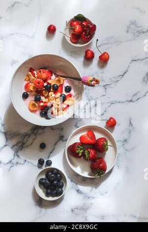 Eine Schüssel Joghurt mit Erdbeeren, Heidelbeeren, Kirschen und Flocken auf einem Marmortisch Stockfoto