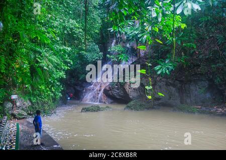 Hübsche Szene eines Wasserfalls, der über Felsen mit einem kleinen See am Fuße der Wasserfälle planscht. Ein kleiner Junge schaut auf. In Jamaika, Der Karibik Stockfoto