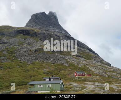 Grüne und rote Holzhütten Hütte am Massiv Trolltindene, Trollwand Trollveggen, im Romsdal Tal, Norwegen. Wolkiger weißer Himmel Wolken. Sommer Stockfoto