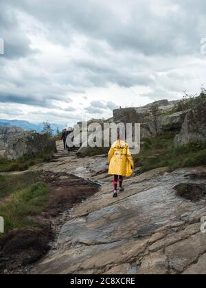 Songesand, Norwegen, 9. September 2019: Junges Mädchen in gelbem Regenmantel auf Wanderung zum Preikestolen massive Klippe berühmte Norwegen Aussichtspunkt Moody Himmel, Herbst Stockfoto