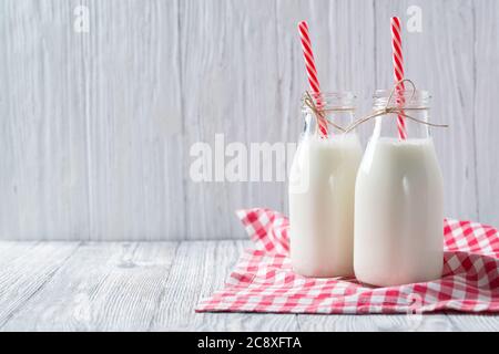 Milchflaschen mit roten Strohhalmen und kariertem Handtuch auf Holzhintergrund Stockfoto