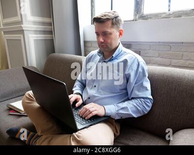 Ein Mann sitzt zu Hause auf der Couch und tippt auf einem Laptop. Stockfoto