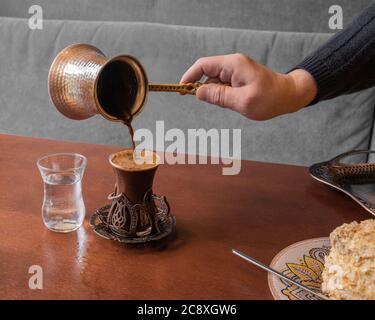 In einem Café wird kräftiger aromatischer türkischer Kaffee mit Schaum aus türke in ein schönes Glas gegossen. Stockfoto