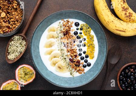 Joghurt-Schale mit Granola und tropischen Früchten auf braunem Hintergrund. Draufsicht. Gesundes vegetarisches Frühstück