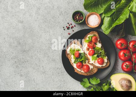 Gesunde vegetarische Bruschetta oder Toast mit gerösteten Tomaten und Ricotta-Käse auf einem schwarzen Teller, Draufsicht, Kopierraum. Italienisches Speisekonzept Stockfoto