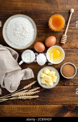 Zutaten zum Backen auf einem Holztisch Hintergrund. Mehl Eier Zucker Butter und Honig. Vertikale Ausrichtung, rustikales Essen Foto. Flach Lay Küche Essen Stockfoto