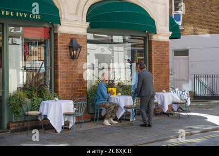 Der Maitre d' begrüßt und setzt zwei Kunden an einem Tisch im Ivy Cafe, Marylebone Lane, London, England, UK Stockfoto