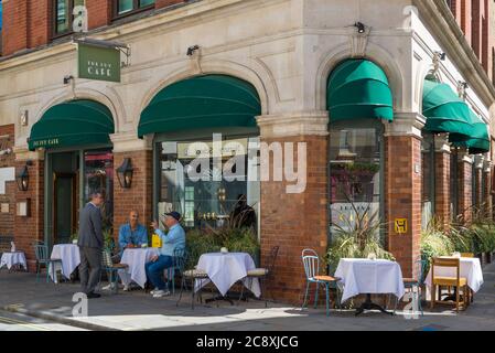 Der Maitre d' begrüßt und setzt zwei Kunden an einem Tisch im Ivy Cafe, Marylebone Lane, London, England, UK Stockfoto