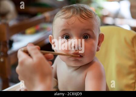 Nahaufnahme Porträt eines niedlichen, plump Baby gefüttert. Verschmiert von Essen auf seinem süßen Gesicht, witziger, verblüffter Ausdruck beim Betrachten der Kamera. Stockfoto