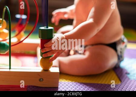 Nahaufnahme der geschwollenen Hand eines schönen, dicken Babys, das mit seinen pädagogischen Spielzeugen aus Farben und Formen spielt. Selektiver Fokus auf den Vordergrund. Stockfoto