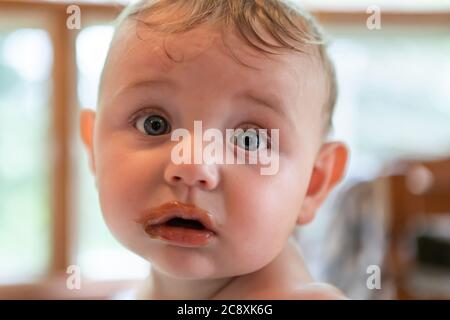 Nahaufnahme Porträt eines niedlichen, plump Baby Blick auf die Kamera mit Flecken von Babynahrung auf seinem süßen Gesicht. Lustig, verblüfft Ausdruck. Stockfoto