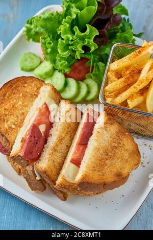 Gegrillter und gepresster Toast mit türkischer Wurst, Käse, Tomaten und Salat auf weißem Teller. Stockfoto