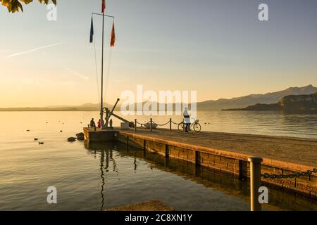 Panoramablick auf den Gardasee mit Menschen auf der Pier bei Sonnenuntergang, Bardolino, Verona, Venetien, Italien Stockfoto