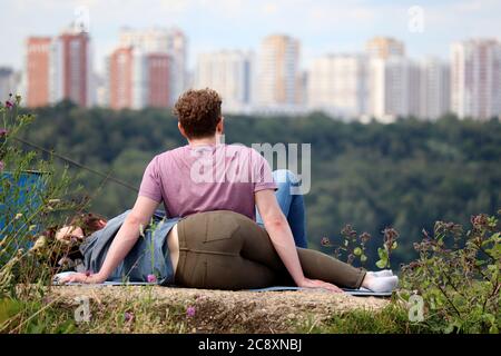 Verliebtes Paar, das auf einem Hügel auf einem Stadthintergrund sitzt. Sommer Freizeit und Entspannung, romantische Datum in einem Park Stockfoto